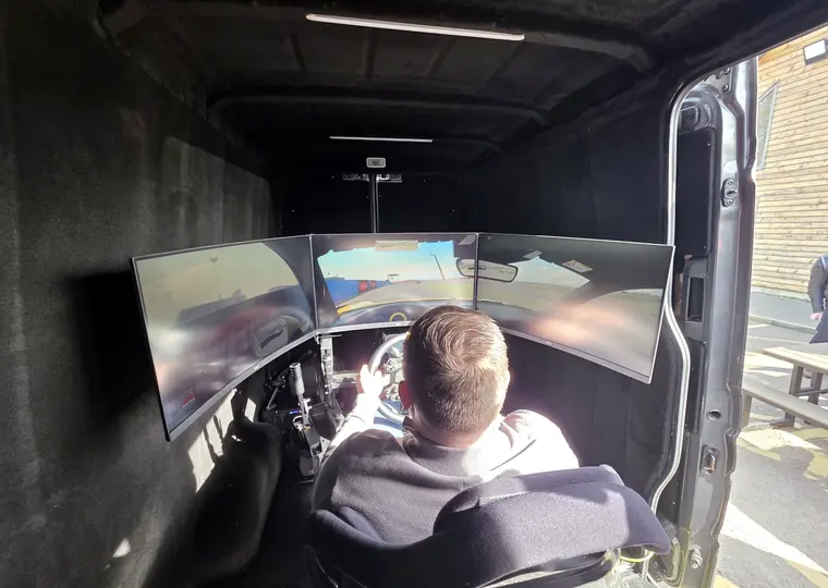 Wide view inside the mobile simulator showing the racing seat, wheel and triple screens.